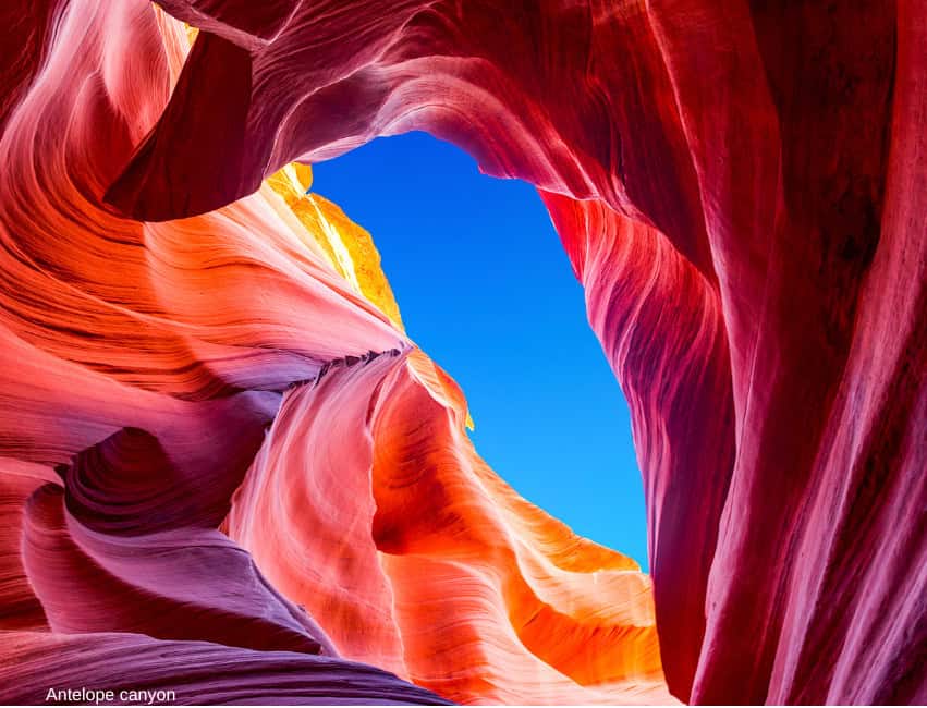 Vivid Antelope Canyon rock formations with bright sunlight and clear blue sky.