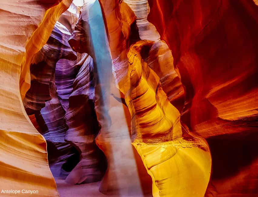 Vivid Antelope Canyon rock formations with bright sunlight and clear blue sky.