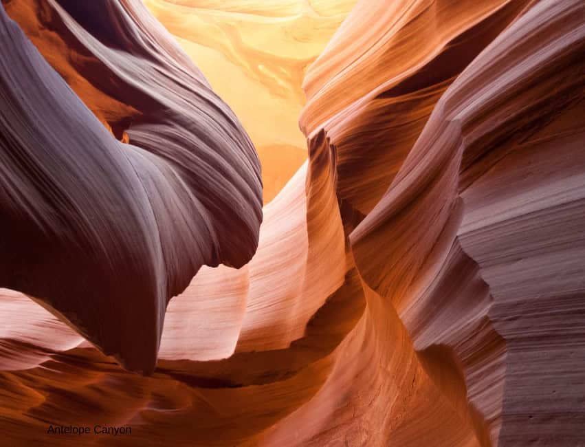Vivid Antelope Canyon rock formations with bright sunlight and clear blue sky.