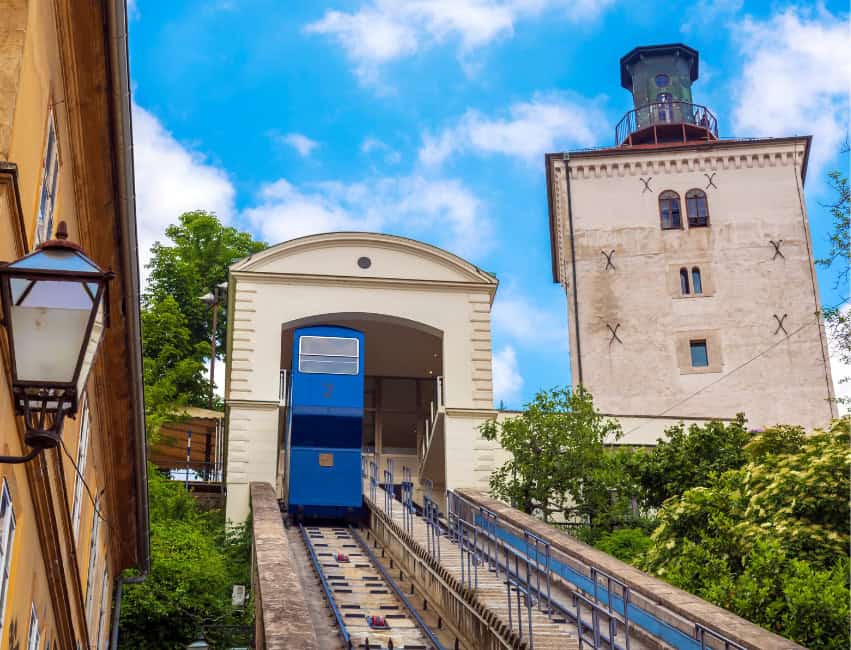 The blue Zagreb Funicular car climbing between Lower and Upper Town with a view of Lotrščak Tower above.”
