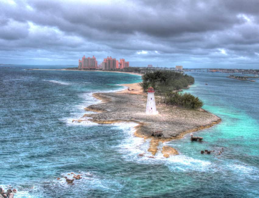 Scenic view of a lighthouse on a coastal island with the ocean and city skyline in the background.
