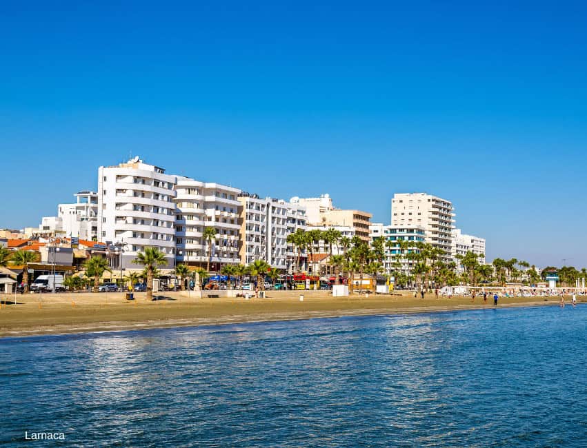Larnaca beachfront with modern hotels and palm trees under clear blue sky.