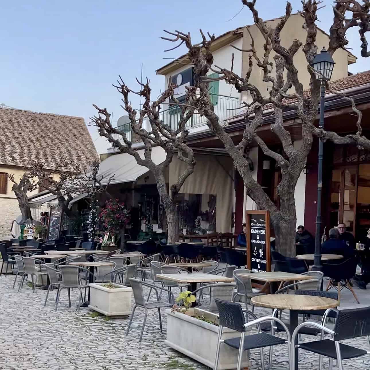 Empty outdoor cafe with leafless trees and stone-paved patio in a quaint European village.