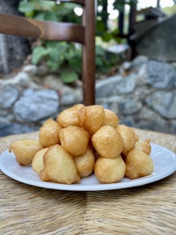 A rustic table with a bowl of golden fried loukoumades drizzled with honey, sprinkled with cinnamon, and a small cup of Cypriot coffee on the side.