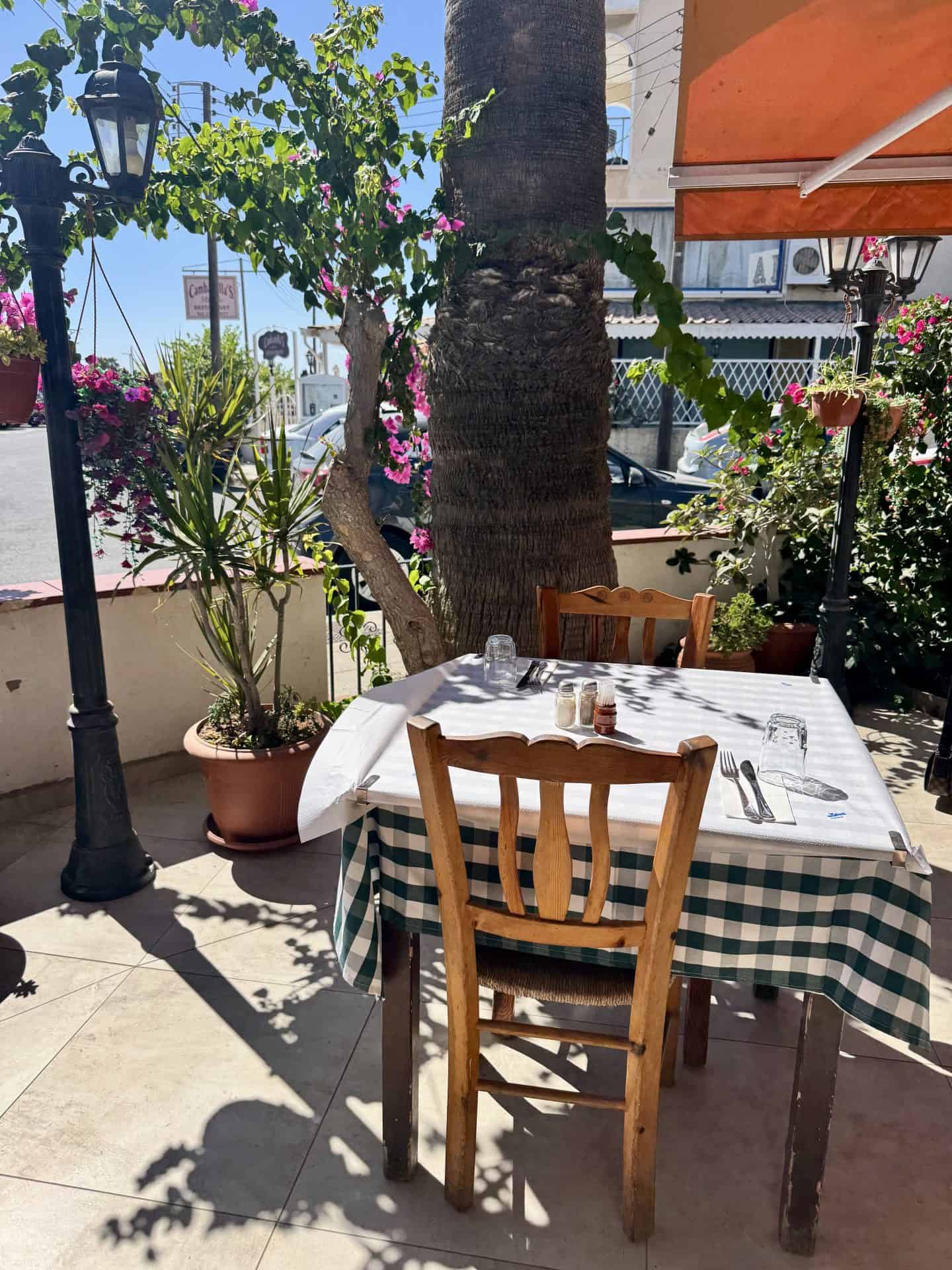 Charming corner table for two with checkered tablecloth, wooden chairs, and bougainvillea flowers at Lysia Meat Tavern in Larnaca, Cyprus