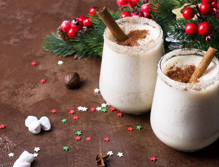 christmas cocktails, glasses of christmas rum eggnog with cocoa powder and cinnamon sticks with christmas decor