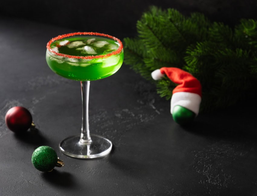grinch christmas cocktails - green grinch martini in glass with ice and mini santa clause hat