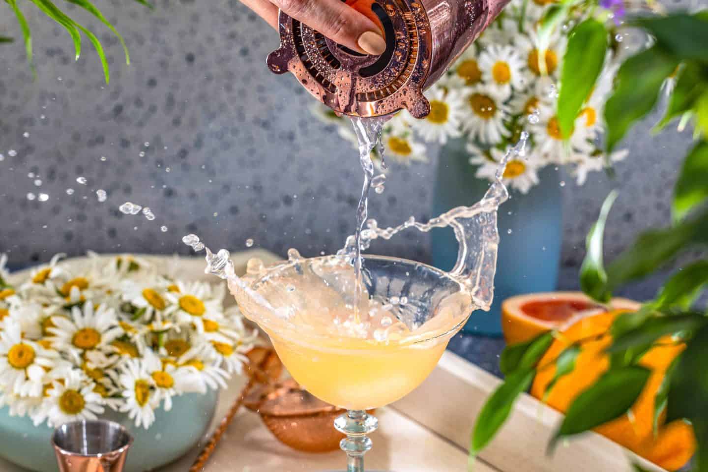 pouring cocktail into cocktail glass splashing with flowers in the background limoncello spritzer