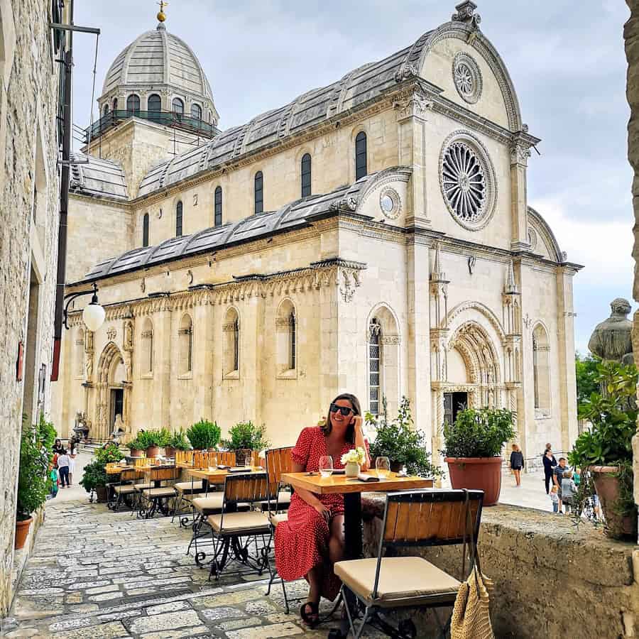 woman in red dress sitting in cafe in front of church in sibenik croatia