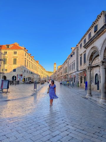 Dubrovnik street scene with historic architecture and a woman enjoying the sunny day.