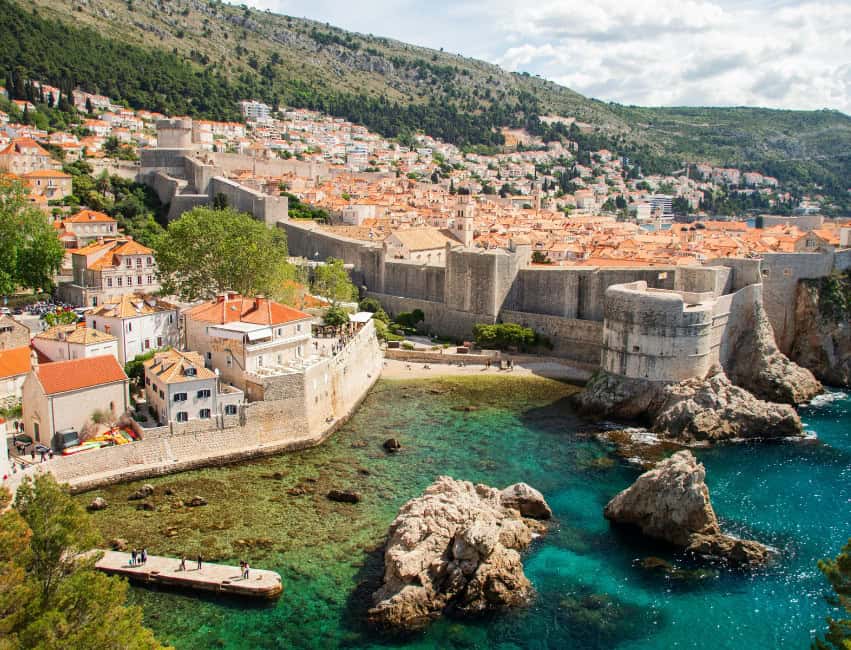 view of Dubrovnik city walls with view of blue water and orange roof tops