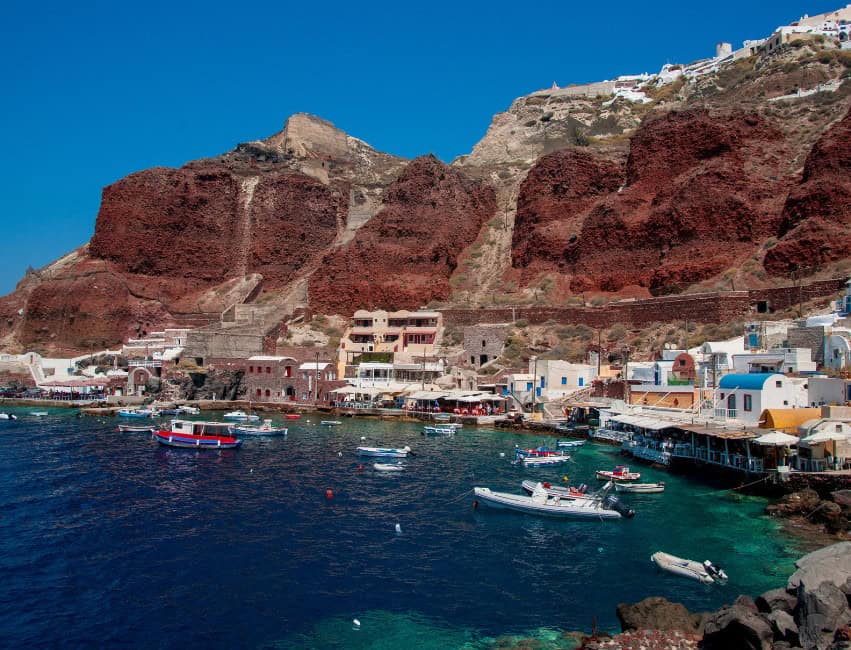 amoudi bay oia santorini greece with boats and mountains in background