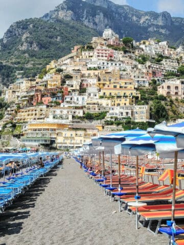 positano italy beach lined with beach chairs and umbrellas with hill town in background