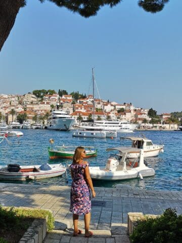 Harbor view of Hvar with boats and a woman in a floral dress enjoying the scenery.