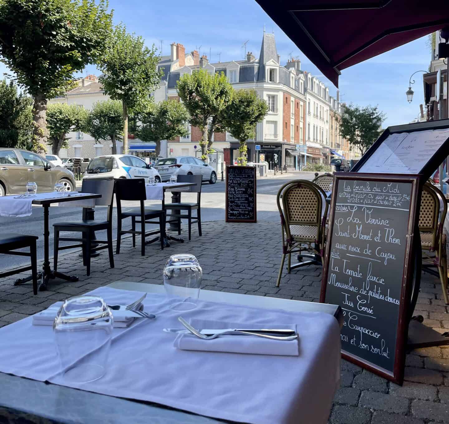 a bistro table with dinner setting with a black board menu in the background in paris