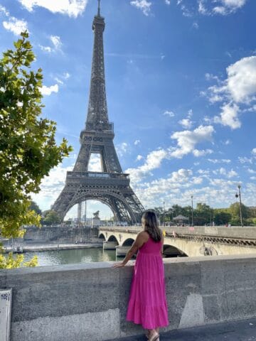 woman in pink dress looking toward the Eiffel Tower on a bright sunny day in Paris